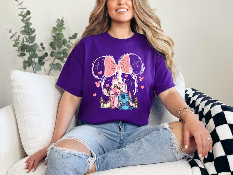 A woman wearing a purple t-shirt with a Disney-themed graphic is sitting on a couch, smiling.