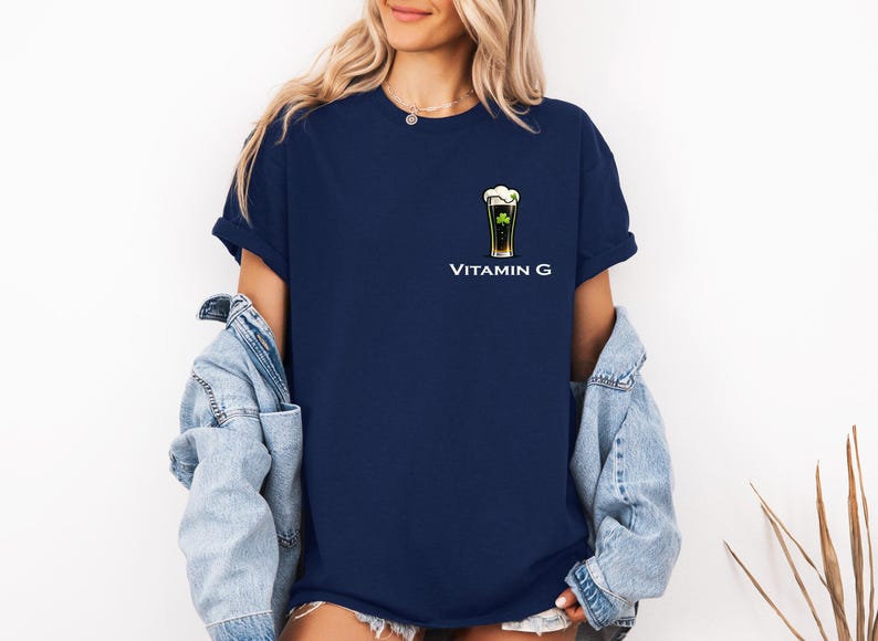 A woman wearing a navy blue t-shirt with a graphic of a beer glass and the text "Vitamin G" printed on it, along with a denim jacket.