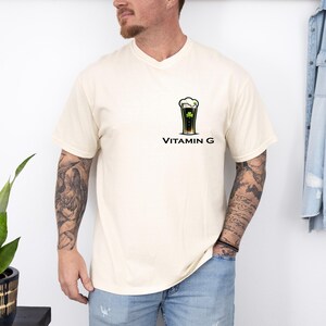 A man wearing a white t-shirt with a graphic of a beer glass and the text "VITAMIN G" stands in front of a white wall.