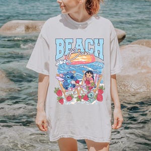 A woman wearing a white t-shirt with a graphic design of a beach scene with a character and strawberries.