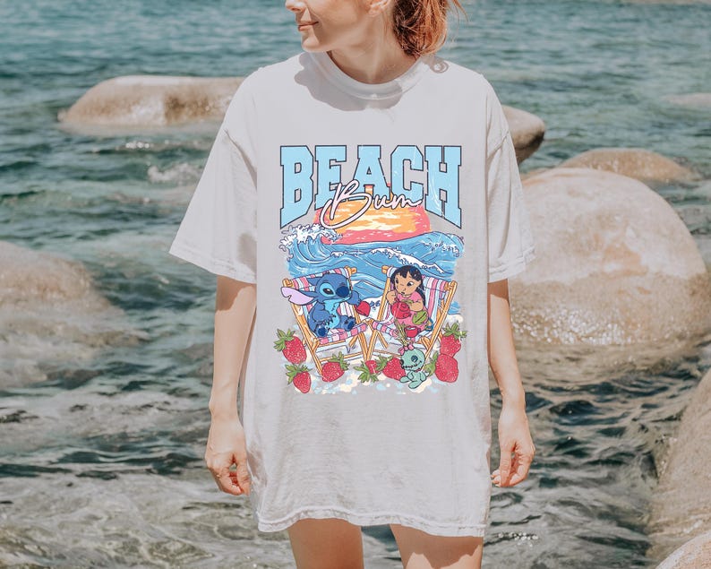 A woman wearing a white t-shirt with a graphic design of a beach scene with a character and strawberries.