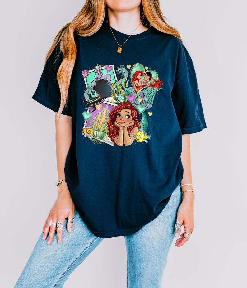 A woman wearing a blue t-shirt with a colorful graphic design featuring characters from the Disney animated film "The Little Mermaid".