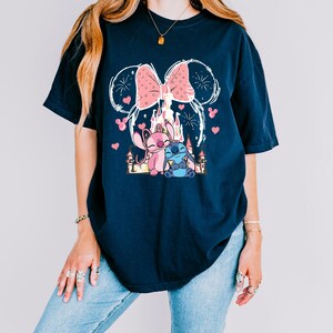 A woman wearing a black t-shirt with a graphic design featuring a castle, a cat, and fireworks.