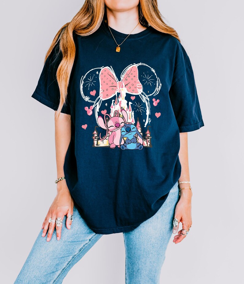 A woman wearing a black t-shirt with a graphic design featuring a castle, a cat, and fireworks.