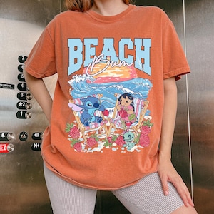 A woman wearing a t-shirt with a beach scene and cartoon characters.
