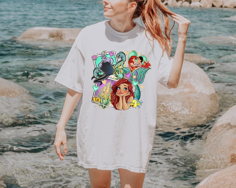 A woman wearing a white t-shirt with a colorful graphic of the mermaid characters from the Disney film "The Little Mermaid".