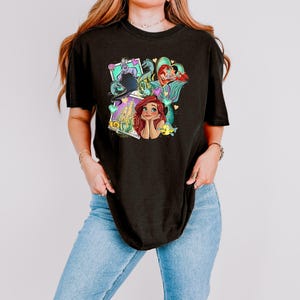 A woman wearing a black t-shirt with a colorful graphic of a mermaid character.