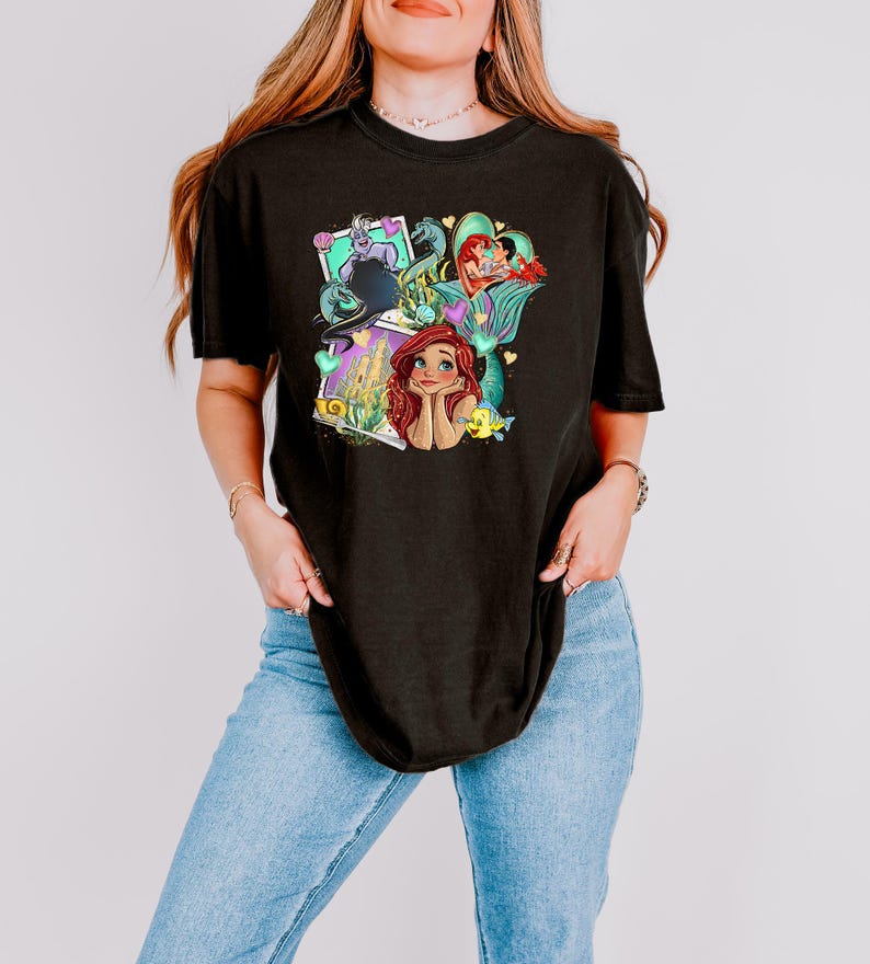 A woman wearing a black t-shirt with a colorful graphic of a mermaid character.