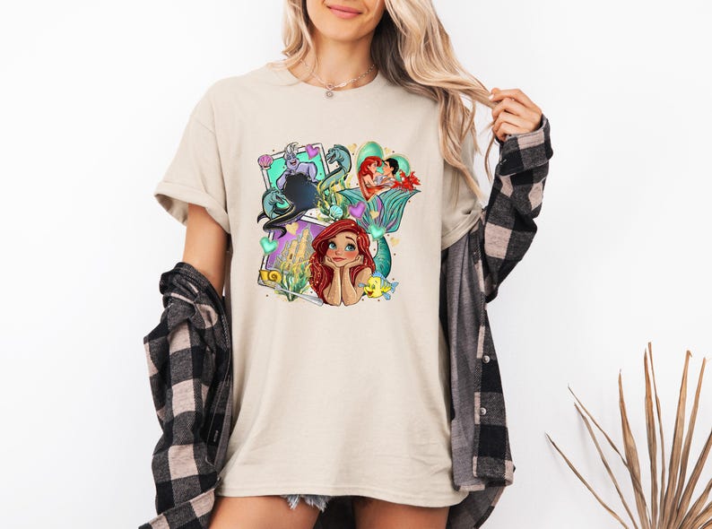 A woman wearing a t-shirt with a colorful graphic of a mermaid character.