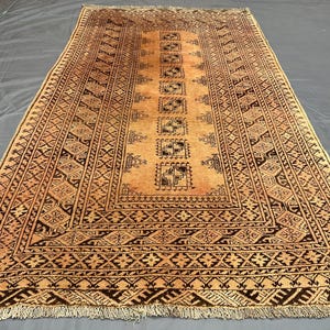 Könnte beinhalten: Rechteckiger Teppich mit einem beigefarbenen Feld und komplizierten dunkelbraunen geometrischen Mustern. Der Teppich hat ein zentrales Design aus sich wiederholenden Quadraten und einen detaillierten Rand. Der Teppich hat einen Fransenrand.