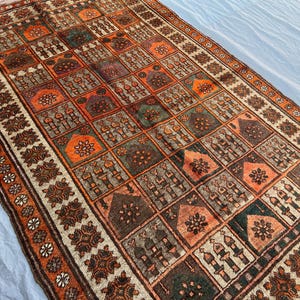 Peut inclure: Tapis rectangulaire tissé à la main avec un motif géométrique. Le tapis présente un motif répétitif de carrés et de motifs floraux dans des tons d'orange, de marron, de vert et de beige. La bordure est marron foncé avec des accents floraux. Le tapis est probablement en laine.