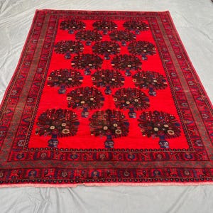 May include: A vibrant red area rug with a repeating pattern of stylized floral arrangements in vases. The rug features a detailed border with intricate designs in shades of brown, blue, and green. The rug's dimensions are approximately 8 x 10 feet.