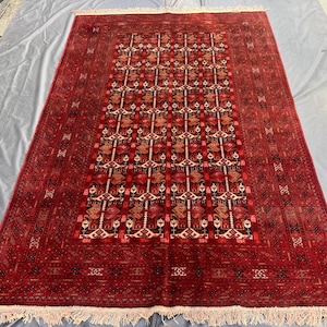 Peut inclure: Un tapis rectangulaire noué à la main, avec un champ rouge profond et des motifs géométriques complexes dans des tons de rouge, de marron et de crème. Le tapis présente un motif de médaillon central et une bordure détaillée avec une frange crème.