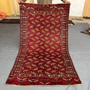 Peut inclure: Un tapis rectangulaire tissé à la main avec un fond rouge foncé et des motifs géométriques complexes dans des tons de marron, beige et blanc. Le tapis présente une bordure détaillée et un champ central rempli de motifs répétitifs.