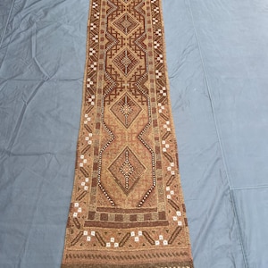 Peut inclure: Un tapis de couloir rectangulaire marron et beige avec un motif géométrique complexe. Le tapis présente des formes de losanges et rectangulaires dans des tons de marron, beige et blanc. Il a une bordure frangée et convient à un couloir ou une entrée.