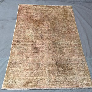 May include: A rectangular, distressed rug with a faded, vintage appearance. The rug features a blend of beige, brown, and muted green tones, creating a textured, aged look. The edges have a subtle fringe detail, adding to the rug's antique aesthetic.