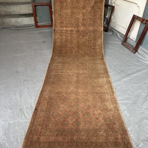 Peut inclure: Un long tapis rectangulaire marron avec un motif floral détaillé. Le tapis a une frange aux deux extrémités et est présenté verticalement. La palette de couleurs comprend des nuances de marron, de beige et des touches de rouge. Le tapis semble être fait d'une matière tissée.