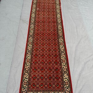 Peut inclure: Un long tapis rectangulaire rouge avec un motif floral complexe. Le tapis a une bordure crème avec un motif floral répétitif et une bordure extérieure rouge. Le tapis est probablement fait de matériau tissé.
