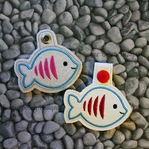 May include: Two white felt fish keychains with blue and red embroidery. The fish have a red and white striped pattern and black eyes. The keychains have a silver metal ring.