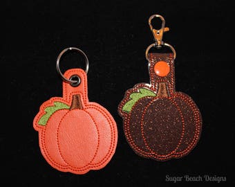 May include: Two pumpkin-shaped keychains, one orange and one brown with glitter. Both have green stems and are attached to silver key rings.