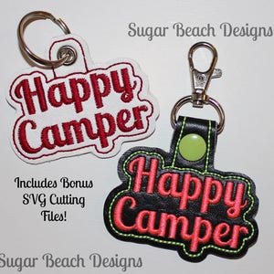 May include: Two keychains with the text "Happy Camper" embroidered on them. One keychain is white with red embroidery and the other is black with pink embroidery. Both keychains have a silver metal ring and a silver metal clasp.