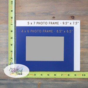 May include: Two picture frames, one blue and one white, with the text "5 x 7 PHOTO FRAME - 9.5" x 7.5"" and "4 x 6 PHOTO FRAME - 8.5" x 6.5"" printed on them. The frames are on a wooden surface.