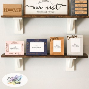 May include: Four wooden picture frames with engraved text and dates. The frames are arranged on a shelf with a wooden sign that reads "Welcome to our nest - The Keane Family". The frames are in various colors, including pink, blue, and gray. The frames are 4x6 inches and 5x7 inches.