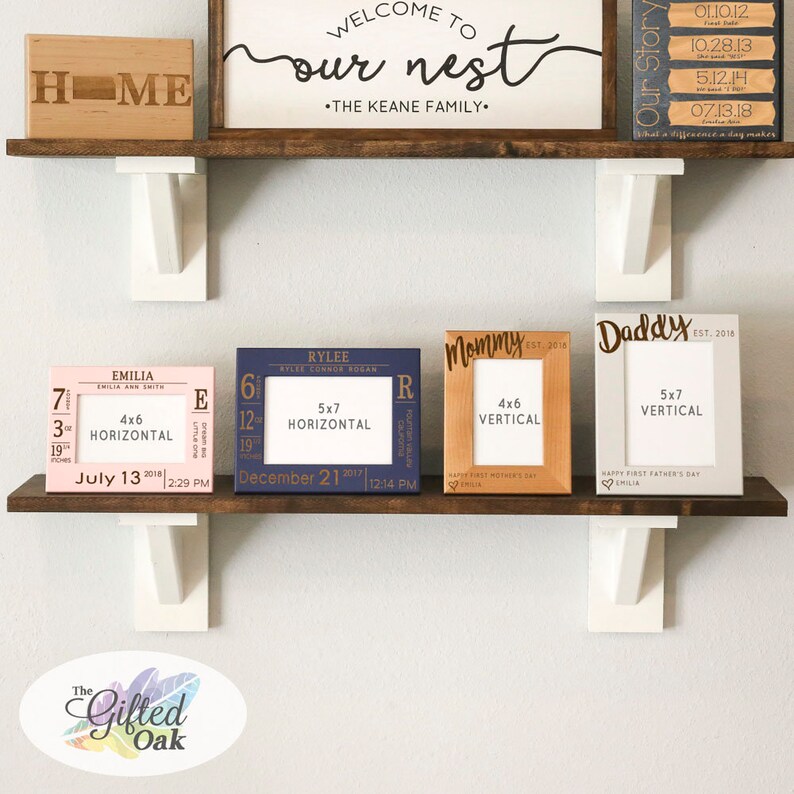 May include: Four wooden picture frames with engraved text and dates. The frames are arranged on a shelf with a wooden sign that reads "Welcome to our nest - The Keane Family". The frames are in various colors, including pink, blue, and gray. The frames are 4x6 inches and 5x7 inches.