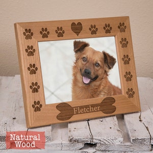 May include: A natural wood picture frame with a heart and paw prints around the border. The frame has a bone-shaped cutout at the bottom with the name "Fletcher" engraved on it.