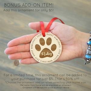 May include: A wooden paw print ornament with the text "Happy Howlidays 2019" and the name "Ruby" engraved on it. The ornament is attached to a red ribbon.