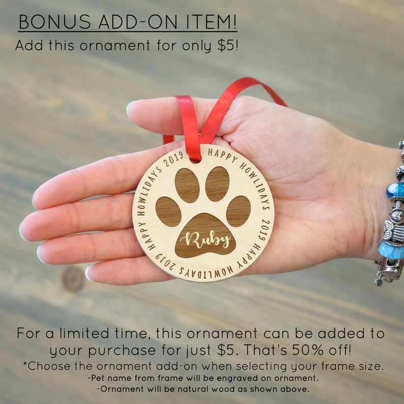 May include: A wooden paw print ornament with the text "Happy Howlidays 2019" and the name "Ruby" engraved on it. The ornament is attached to a red ribbon.