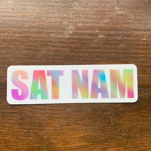 May include: A white sticker with the words "SAT NAM" in rainbow holographic lettering.