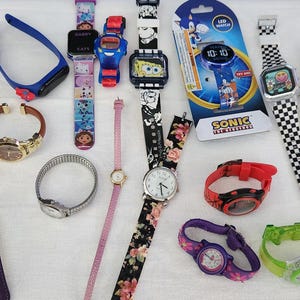 May include: A collection of various wristwatches, including digital and analog styles. Designs include floral patterns, cartoon characters, and checkerboard straps. Colors range from red and purple to black and white. Some watches have metal bands, while others have silicone or fabric straps.