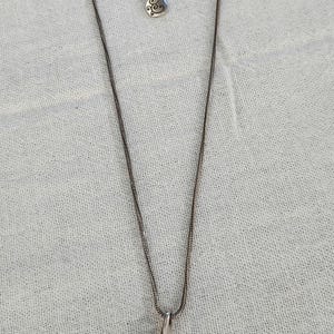 May include: Silver-toned necklace with a teardrop pendant. The pendant features an engraved swirl design. The necklace has a delicate chain and an adjustable length. A small charm hangs near the clasp.