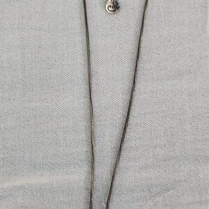 May include: Silver-toned necklace with a teardrop pendant. The pendant features an etched swirl design. The necklace has an adjustable chain and a small charm near the clasp. The background is a light gray fabric.