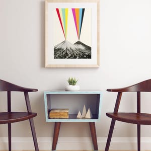 Puede incluir: Una impresi&oacute;n enmarcada de dos monta&ntilde;as con un arco&iacute;ris colorido que emana de las cumbres. La impresi&oacute;n est&aacute; colgada en una pared blanca sobre una mesa auxiliar azul claro con un libro y formas de madera decorativas. Dos sillas de madera est&aacute;n a cada lado de la mesa.
