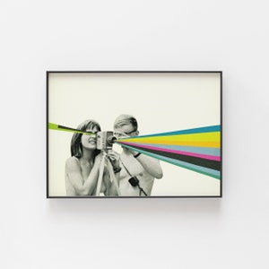 May include: A black and white photograph of a couple using a vintage camera. The camera is pointed towards the viewer and a rainbow of colours shoots out of the lens.
