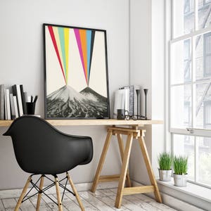 Puede incluir: Una impresi&oacute;n enmarcada en negro de una cordillera con rayos de luz de colores que brillan sobre ella. La impresi&oacute;n est&aacute; colgada en una pared blanca sobre un escritorio de madera con una silla negra y una planta en maceta.
