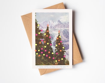May include: A vintage Christmas card with a mountain backdrop and decorated fir trees. The trees are decorated with neon pink, orange, and yellow baubles. The card is set against a brown envelope, evoking a festive holiday atmosphere.