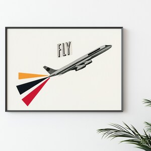 May include: A framed print of a black and white airplane with the word "FLY" in a black rectangle on a white background. The airplane is flying upwards and has a red, black, and orange trail behind it.