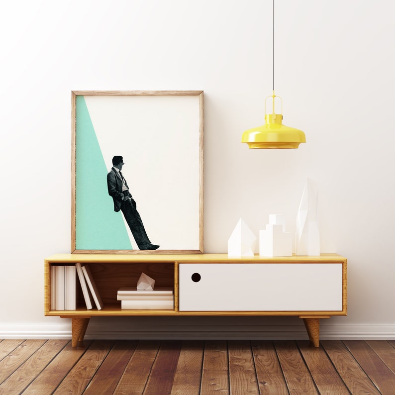 May include: A mid-century modern style wooden media console with a white drawer and open shelves. The console is decorated with a framed print of a man in a suit standing on a teal and white geometric background. A yellow pendant light hangs above the console.