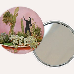 Op de afbeelding: Een ronde compact spiegel met een roze achtergrond en een silhouet van een persoon die in een plantenbak staat vol met vetplanten en cactussen.