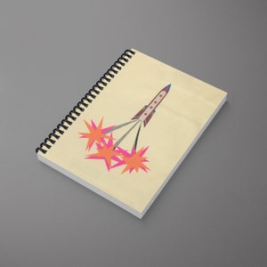 Peut inclure: Un carnet à spirales jaune avec une illustration de fusée. La fusée est rouge, bleue et blanche avec des étoiles roses et orange autour.