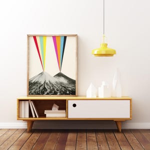 Puede incluir: Una impresi&oacute;n enmarcada de una escena de monta&ntilde;a abstracta colorida con un efecto arco&iacute;ris. La impresi&oacute;n se muestra en un estante de madera con un caj&oacute;n blanco y una luz colgante amarilla arriba.