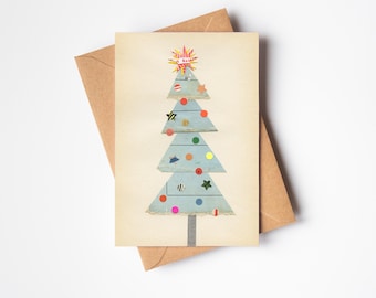May include: A Christmas card with a light blue tree design, decorated with colourful circular and star ornaments. The tree is on a cream background, with a brown envelope behind it. The tree has a starburst at the top.