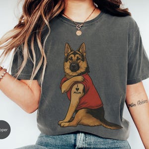German Shepherd dog illustration wearing a red shirt, lifting sleeve to reveal “I love mom” tattoo, vintage style retro pet graphic, bold clean lines, centered composition, perfect for dog lovers and animal themed apparel designs