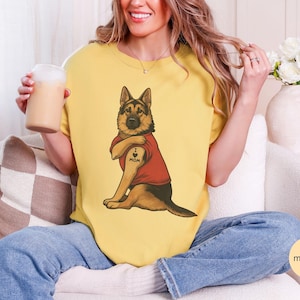 German Shepherd dog illustration wearing a red shirt, lifting sleeve to reveal “I love mom” tattoo, vintage style retro pet graphic, bold clean lines, centered composition, perfect for dog lovers and animal themed apparel designs