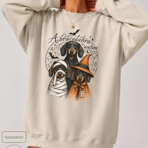 Dachshund Halloween long sleeve and sweatshirt design with three black and tan dogs, mummy wraps, orange witch hat, bats and spell symbols.