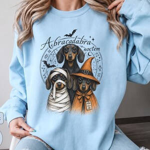 Dachshund Halloween long sleeve and sweatshirt design with three black and tan dogs, mummy wraps, orange witch hat, bats and spell symbols.