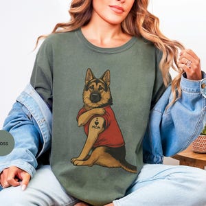 German Shepherd dog illustration wearing a red shirt, lifting sleeve to reveal “I love mom” tattoo, vintage style retro pet graphic, bold clean lines, centered composition, perfect for dog lovers and animal themed apparel designs